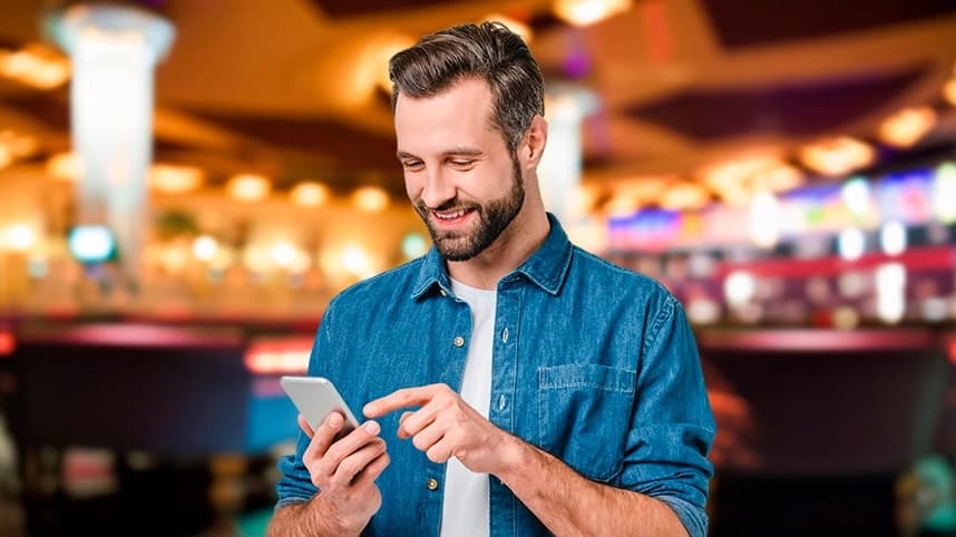 Image shows a men smiling while use his smartphone in a casino.